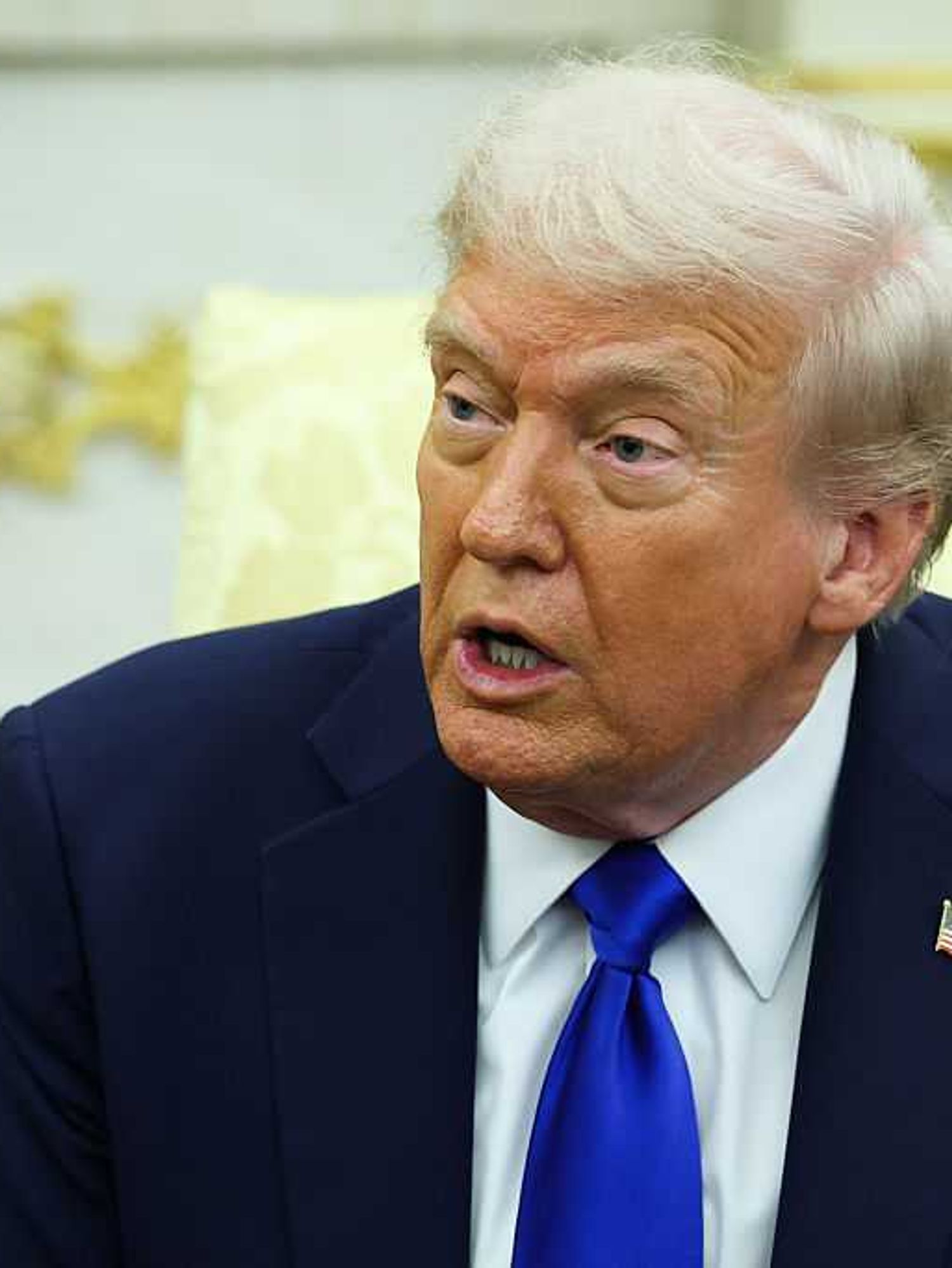 Donald Trump sitting on a cream chair and speaking in the Oval Office.