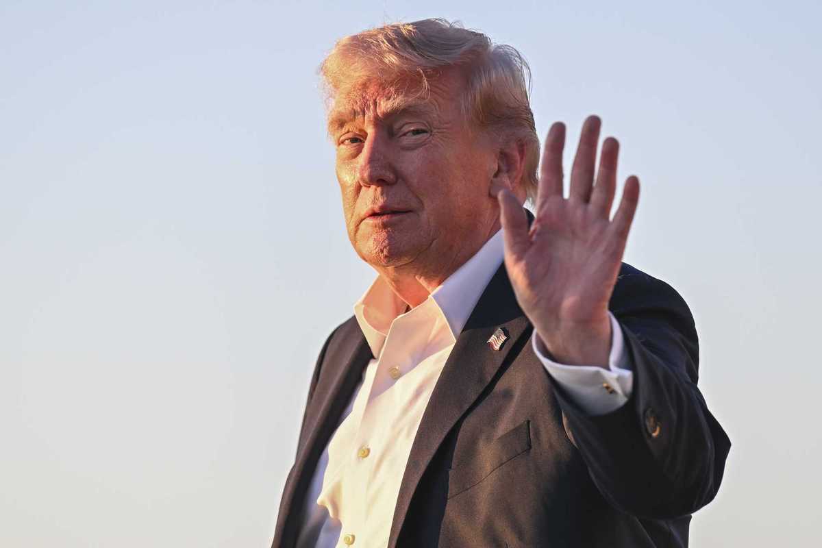 Donald Trump smiles and holds up his left hand while his face is lit up by the glow of the Sun.