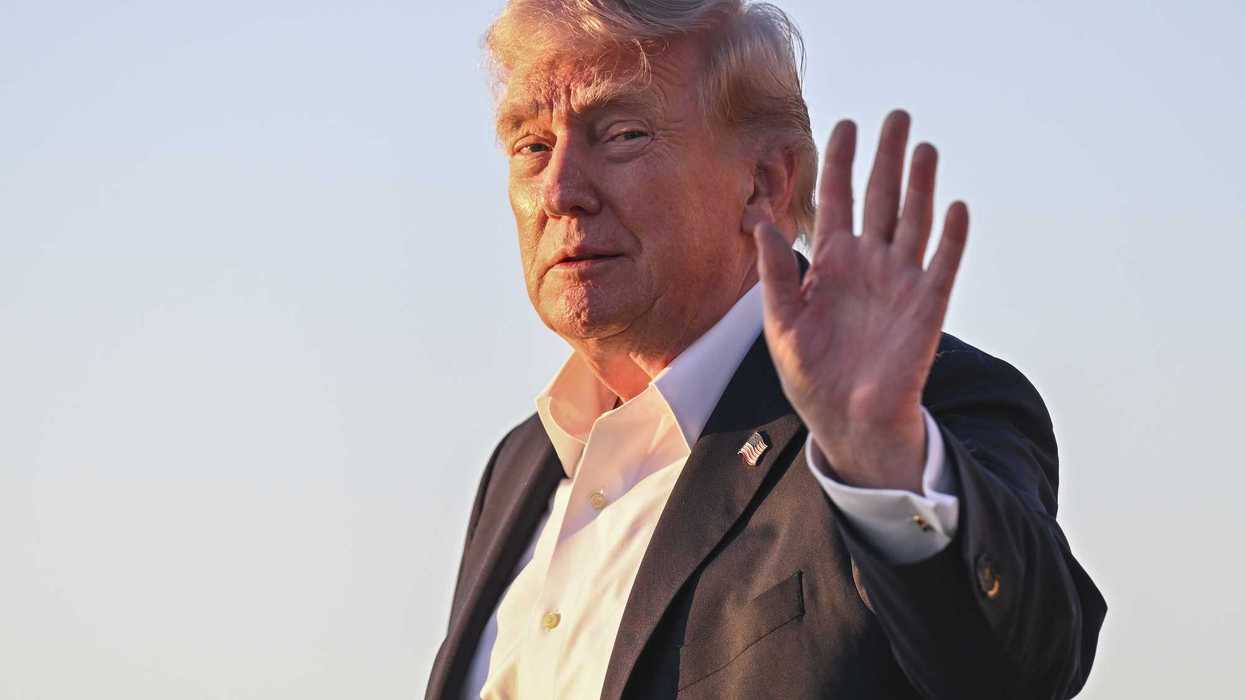 Donald Trump smiles and holds up his left hand while his face is lit up by the glow of the Sun.