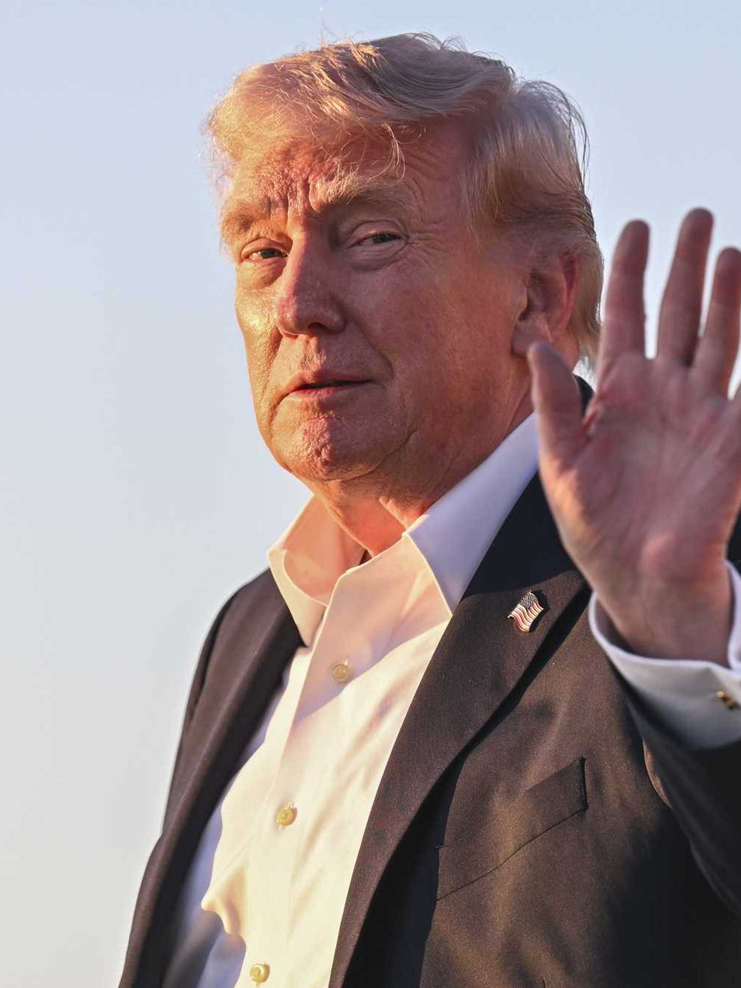 Donald Trump smiles and holds up his left hand while his face is lit up by the glow of the Sun.