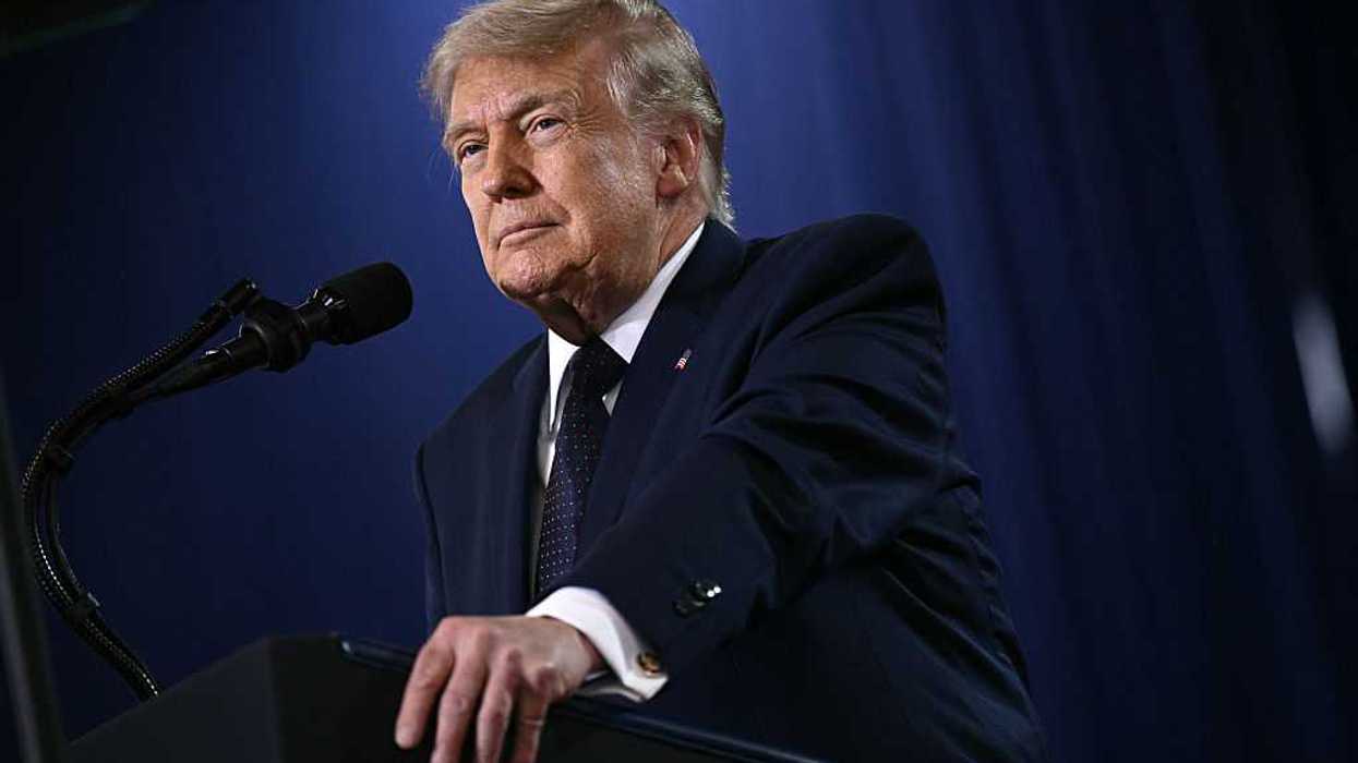 Donald Trump smiles as he speaks behind a black lectern.