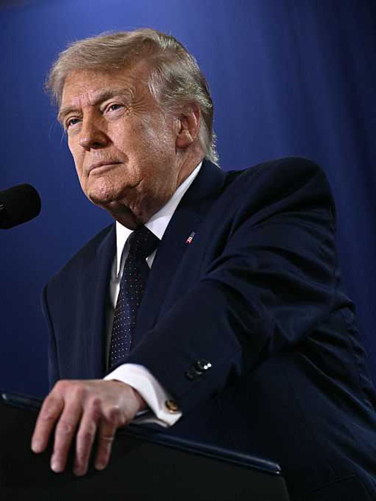 Donald Trump smiles as he speaks behind a black lectern.