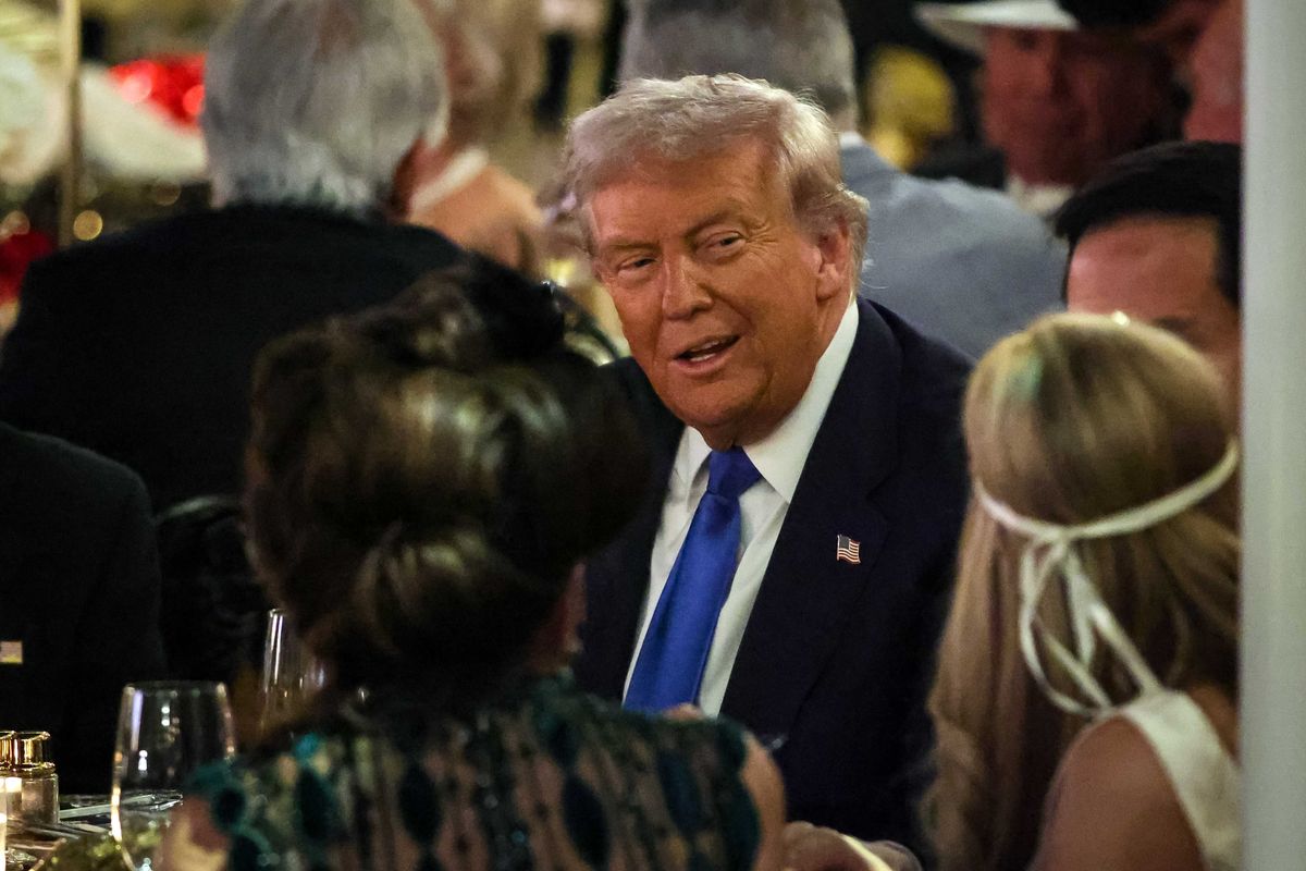Donald Trump smiles at dinner guests while sat at a table at a Mar-a-Lago party.