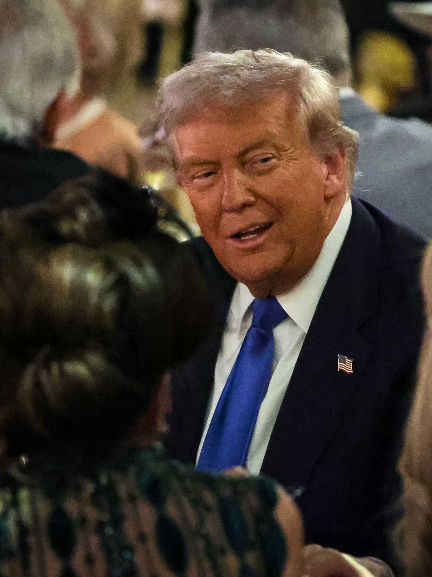 Donald Trump smiles at dinner guests while sat at a table at a Mar-a-Lago party.