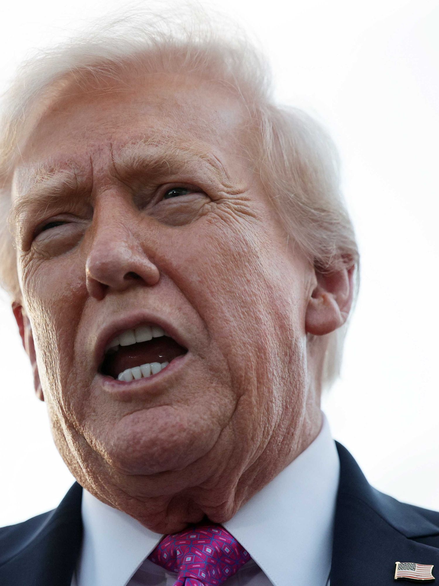 Donald Trump speaking outside against a bright white sky.