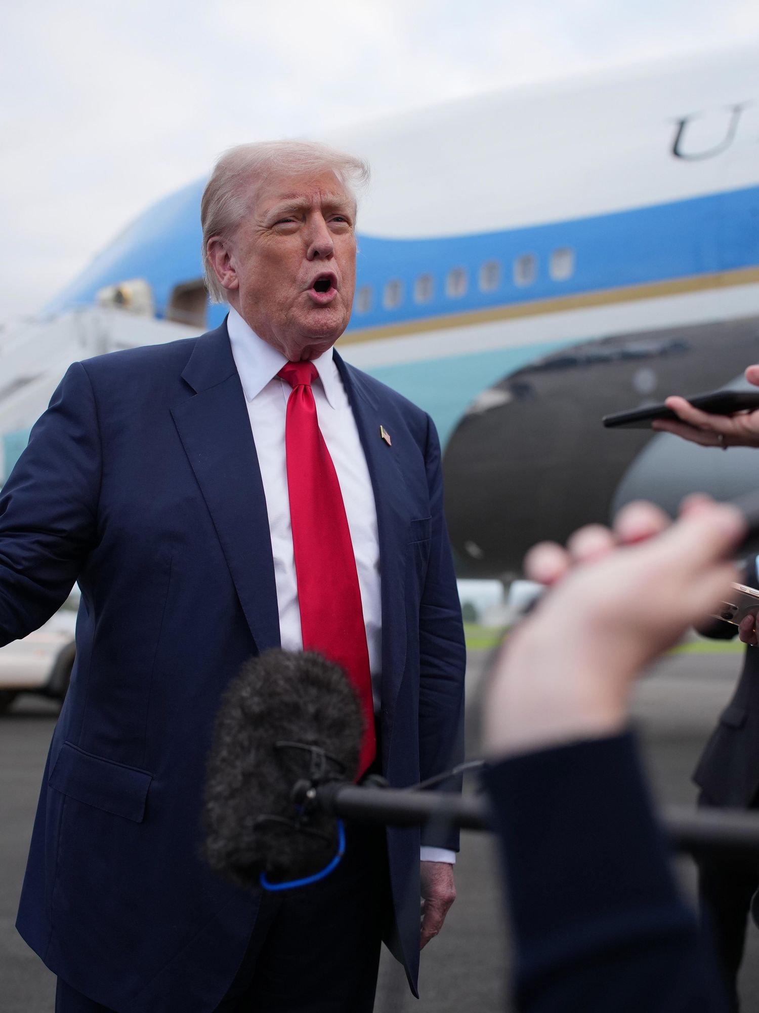 Donald Trump speaks to reporters at Glasgow Prestwick airport, with Air Force One visible in the background.
