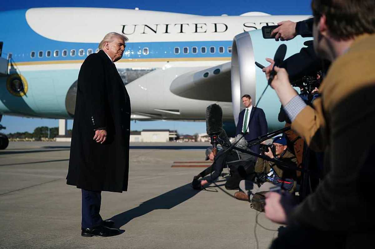 Donald Trump speaks to the media before boarding Air Force One, which is seen behind him.