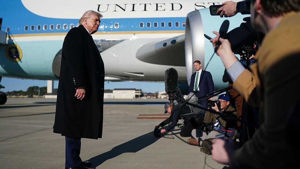 Donald Trump speaks to the media before boarding Air Force One, which is seen behind him.