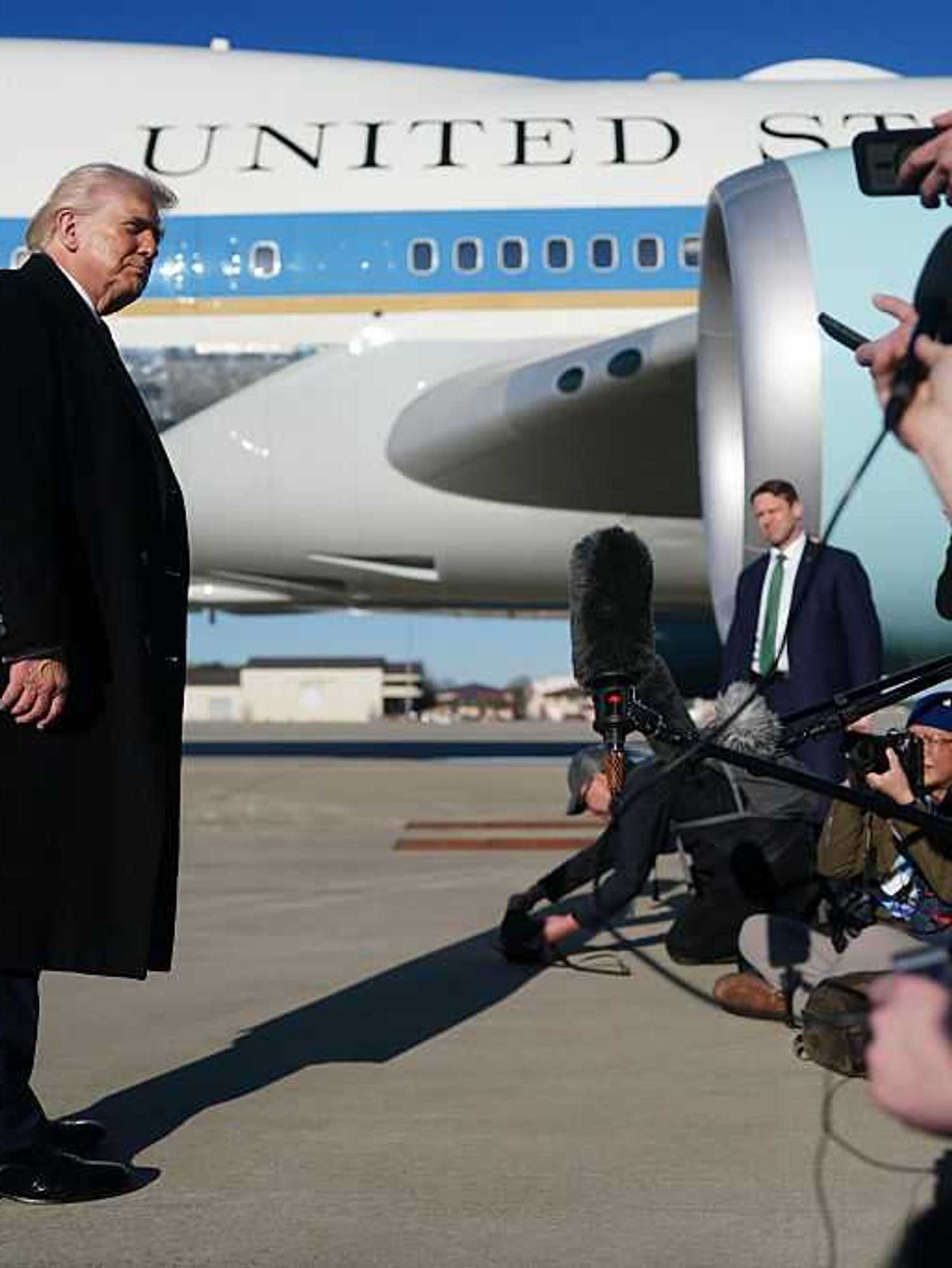 Donald Trump speaks to the media before boarding Air Force One, which is seen behind him.