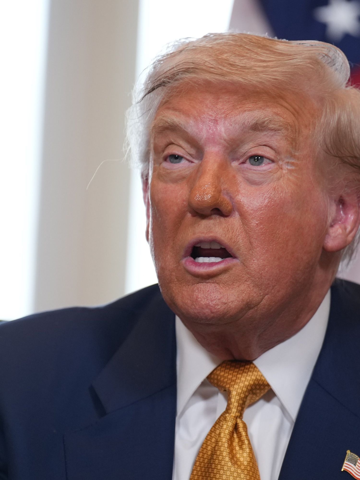 Donald Trump speaks to the press in front of an American flag.
