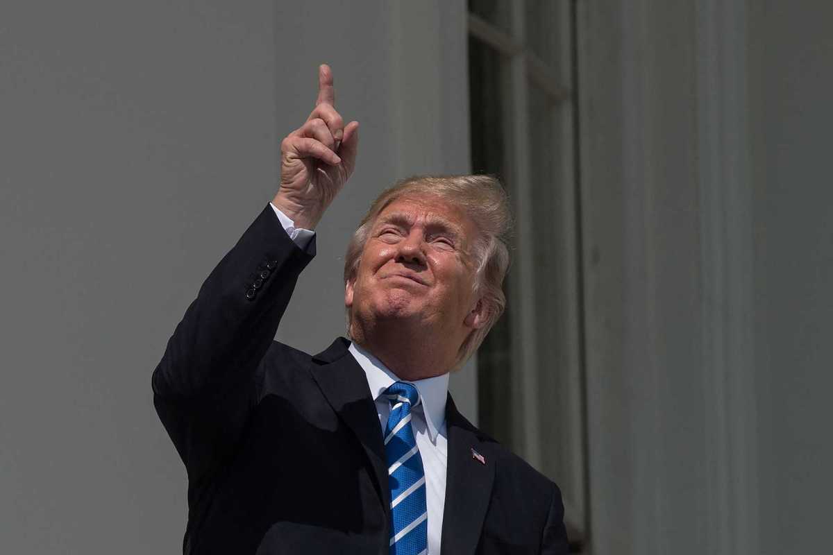 Donald Trump squints and points upwards at the sun while watching the solar eclipse from a White House balcony in 2017.