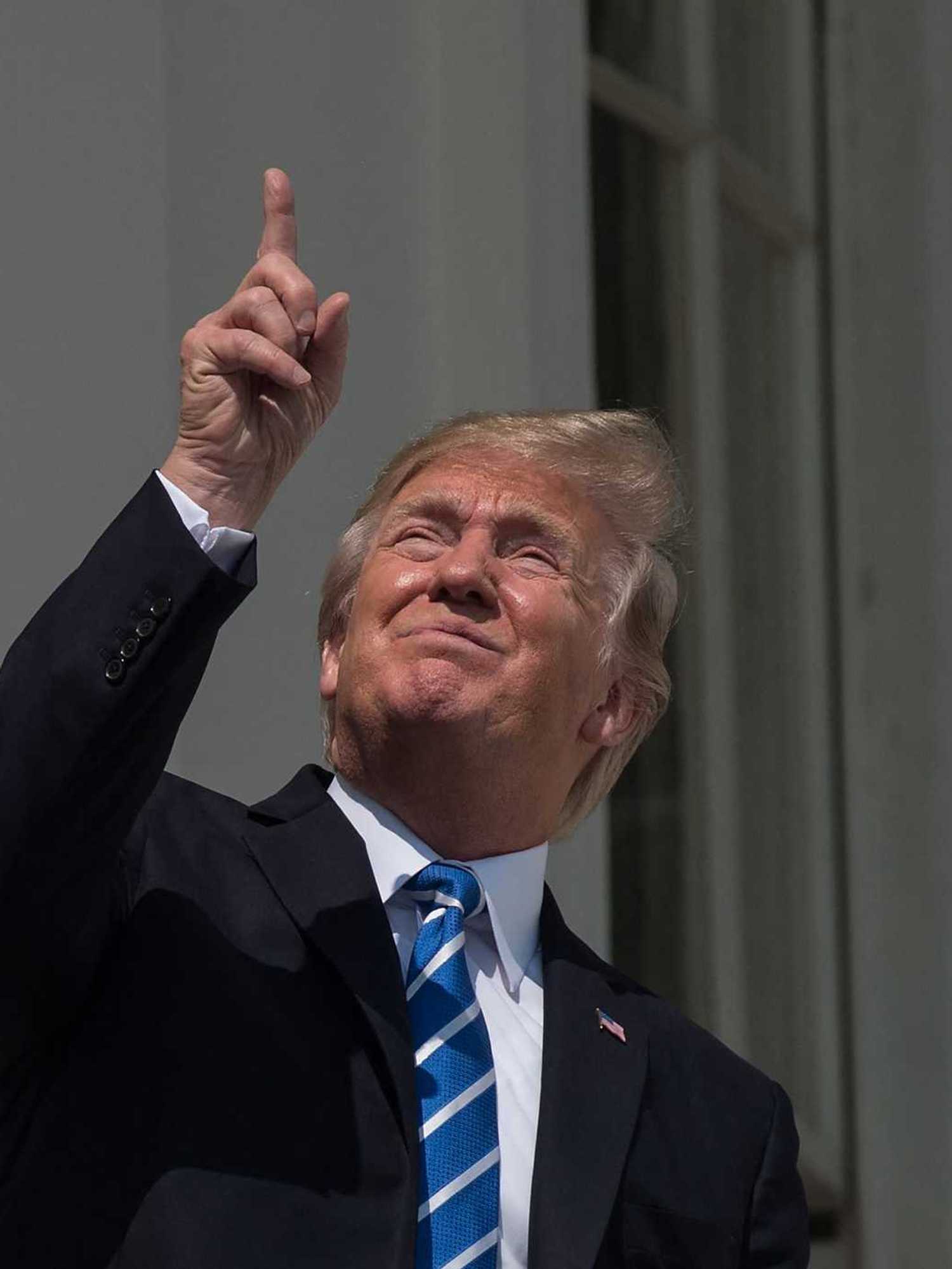 Donald Trump squints and points upwards at the sun while watching the solar eclipse from a White House balcony in 2017.