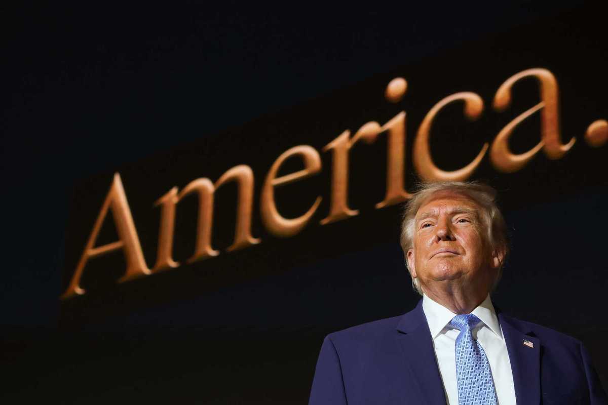 Donald Trump standing in front of a screen with the word 'America' on it.