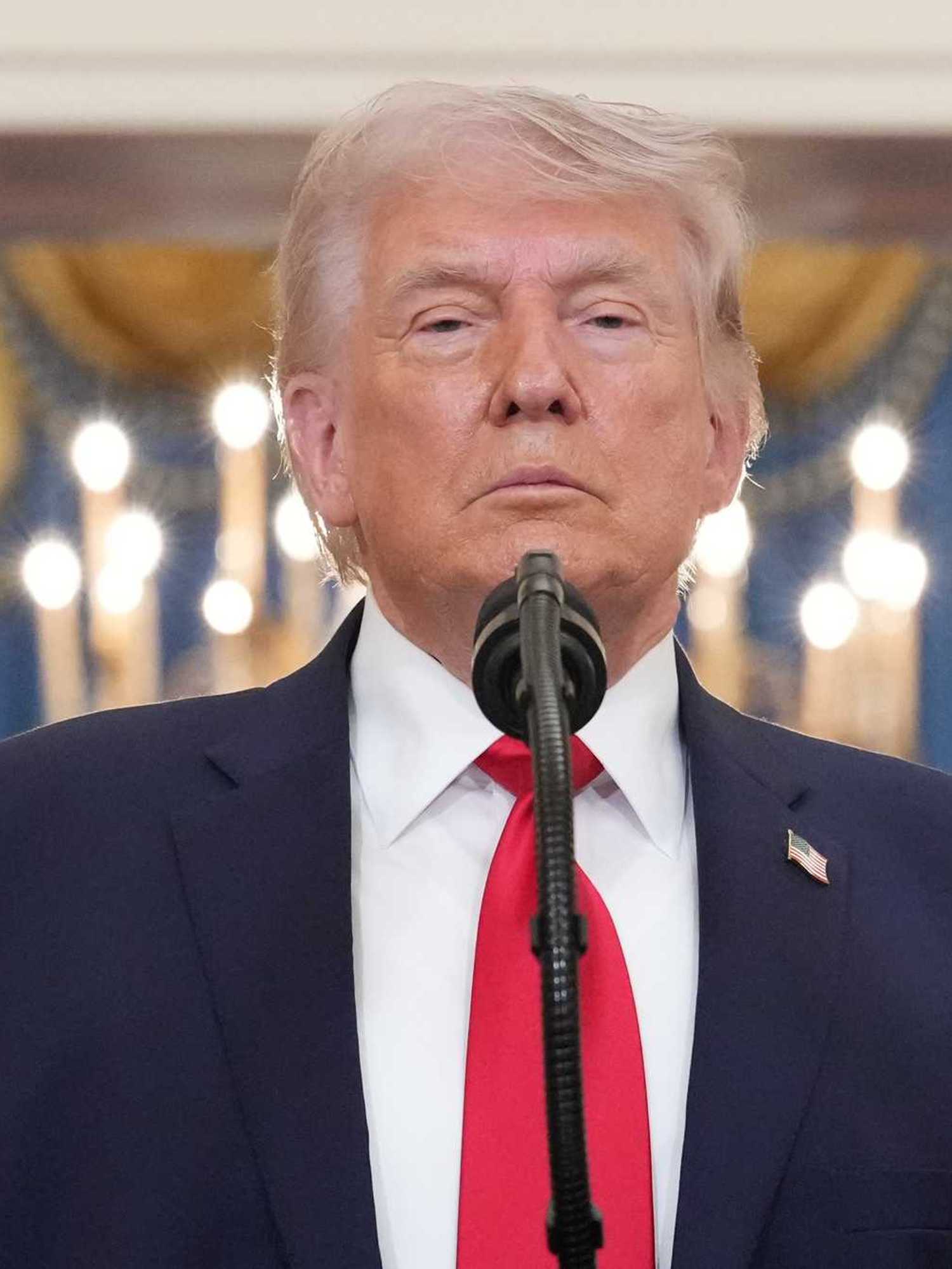 Donald Trump stands behind a microphone and looks directly into the camera.