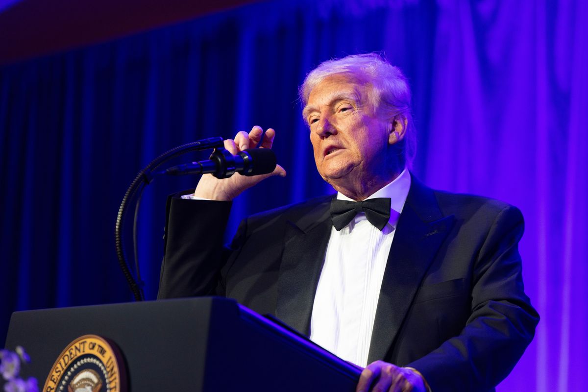 Donald Trump stands behind his presidential lectern and adjusts the microphone with his right hand while speaking.