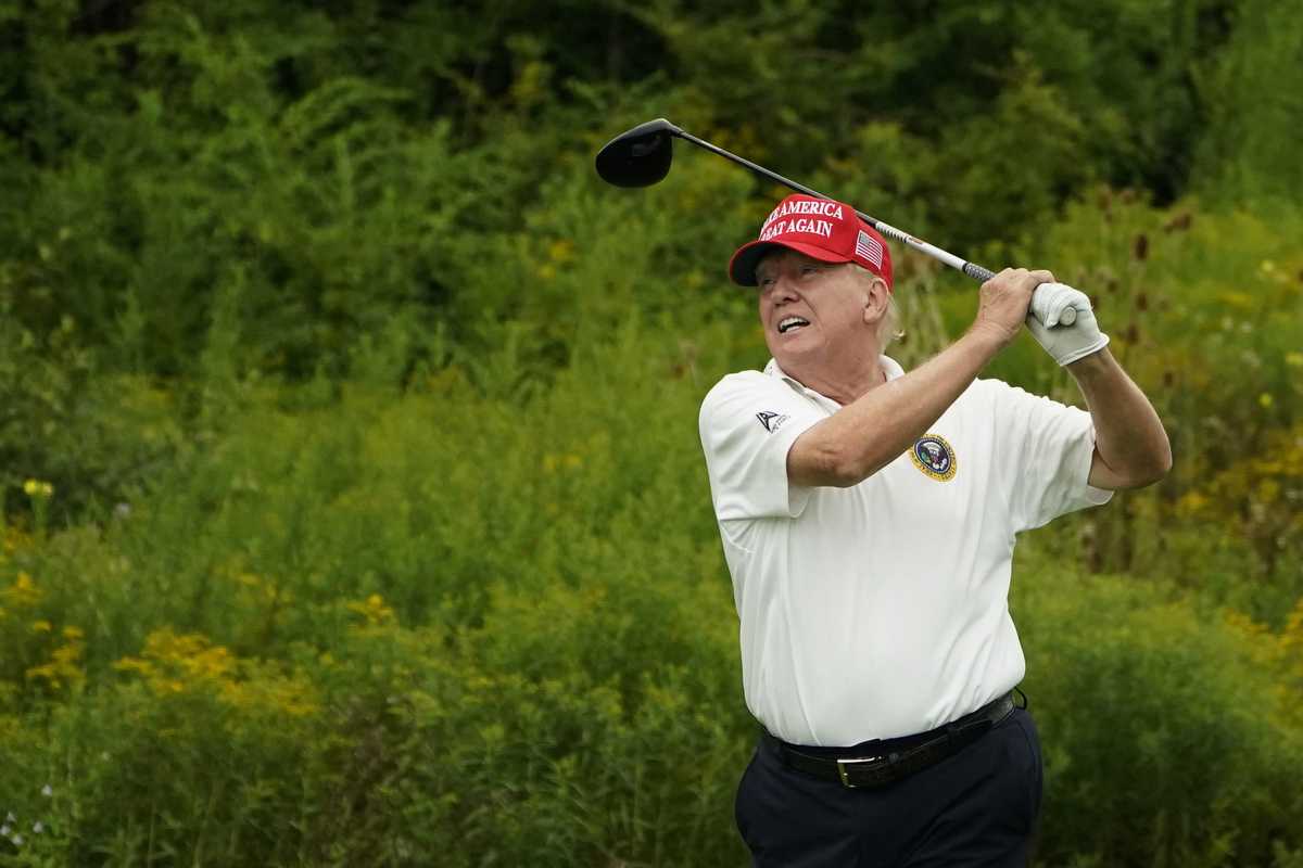 Donald Trump swinging a golf club on a golf course.