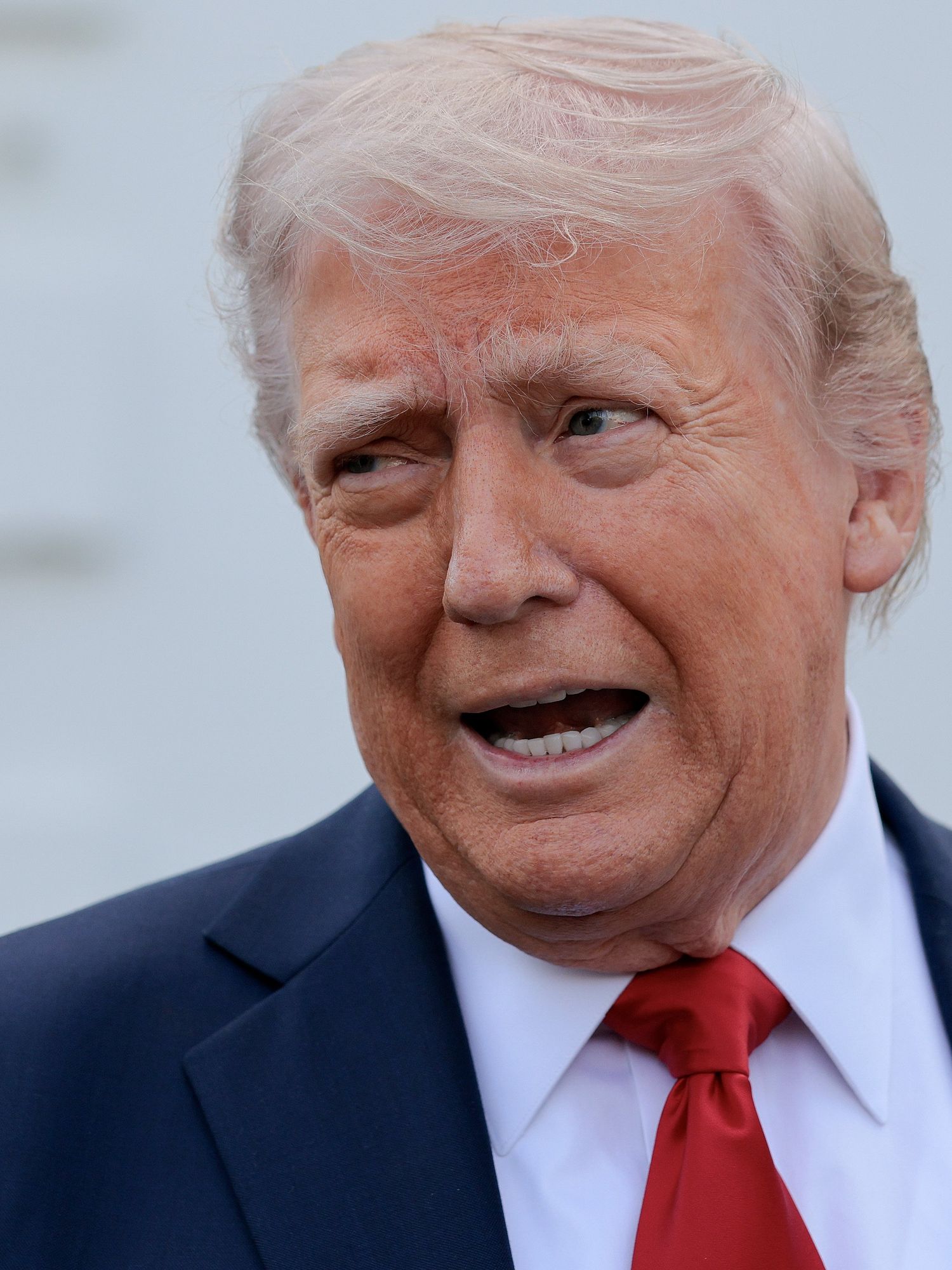 Donald Trump talking, wearing a dark blue suit and red tie.