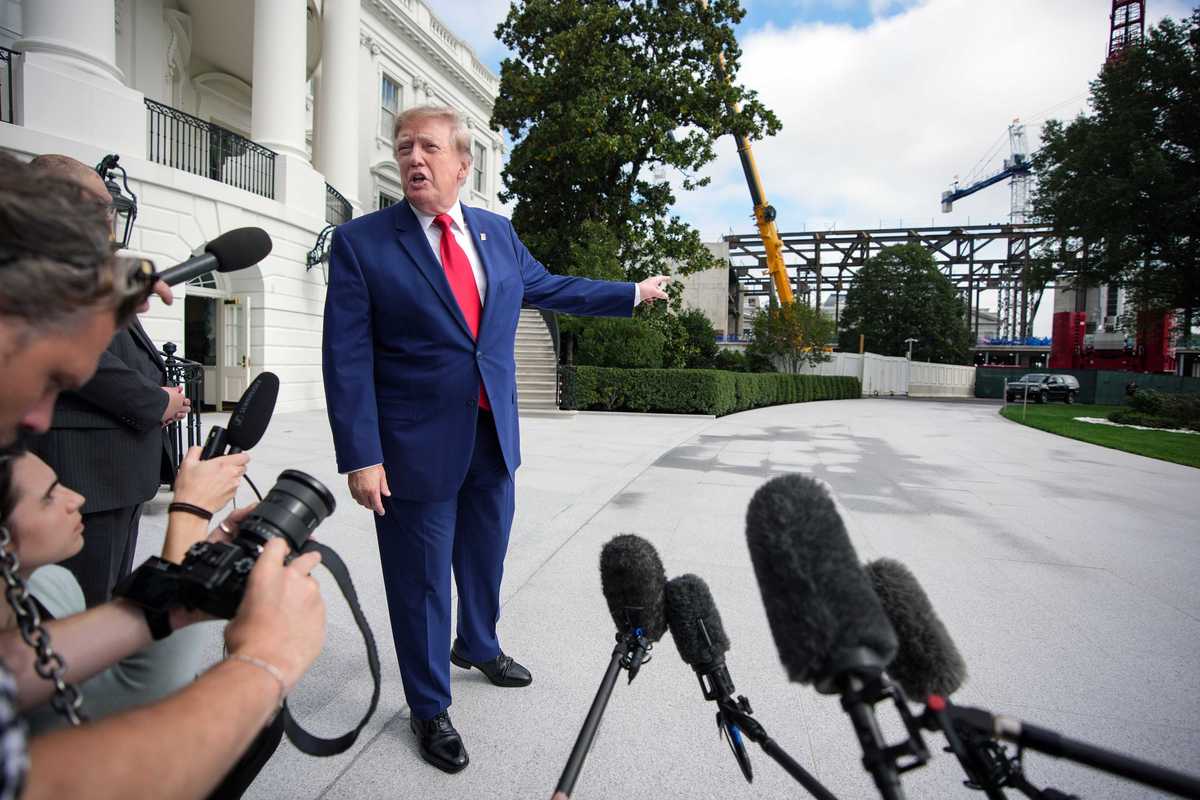 Donald Trump talks to reporters and points to the construction of the White House ballroom behind him.