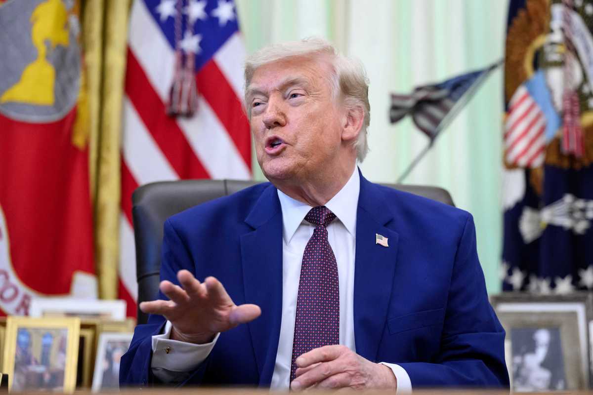 Donald Trump talks to reporters in the Oval Office while sat behind the Resolute Desk.