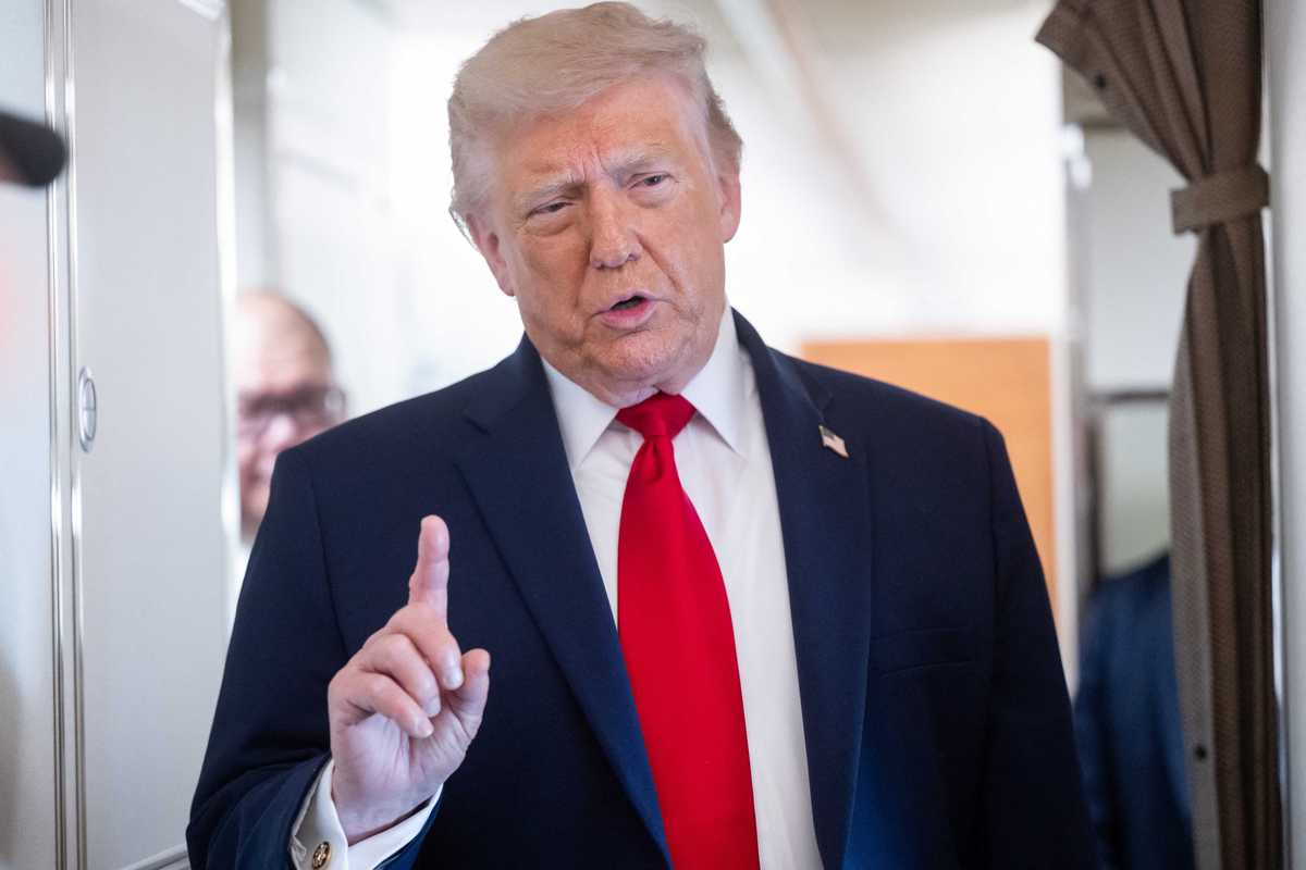 Donald Trump talks to the press on board Air Force One, raising his right index finger.