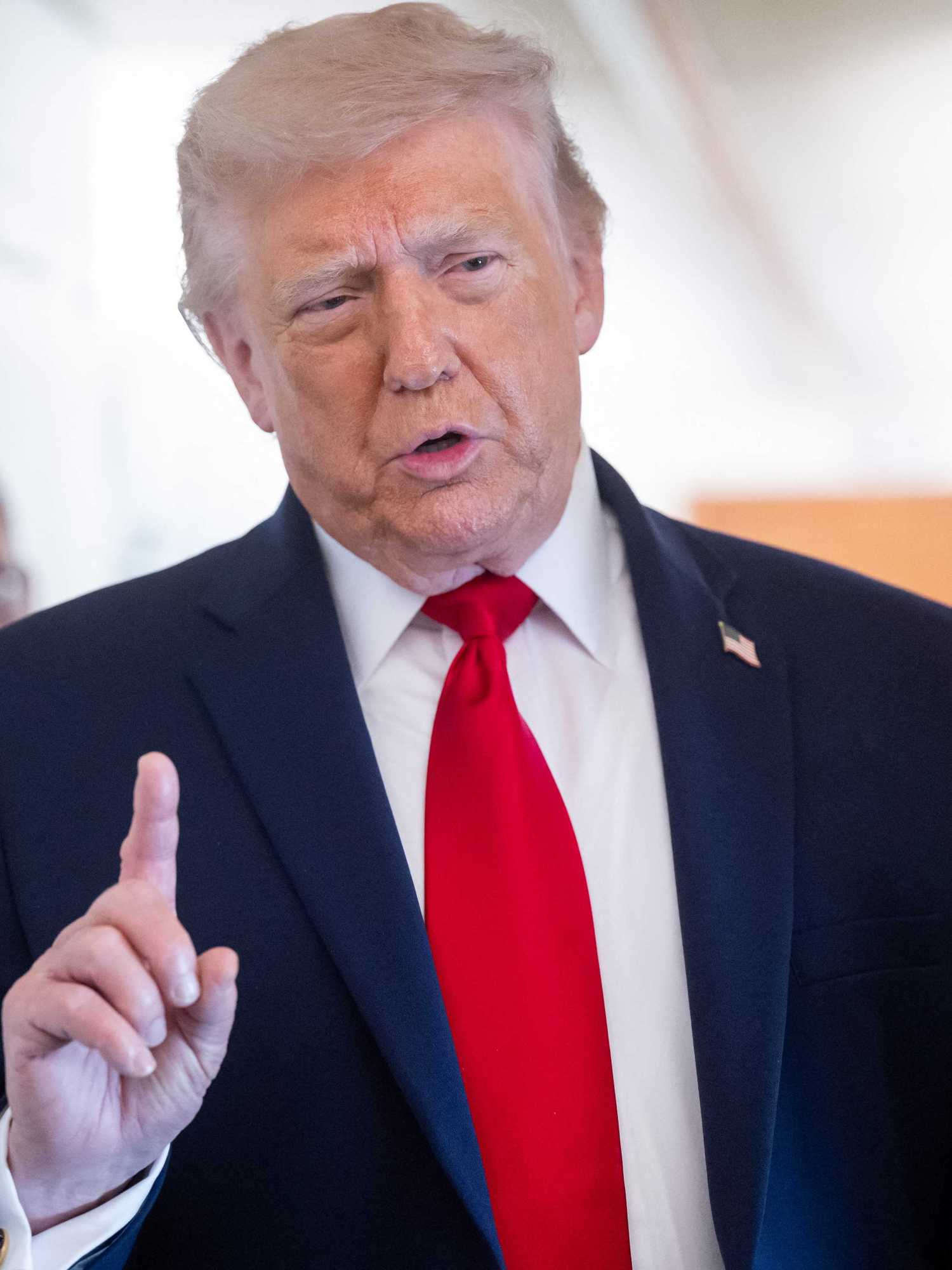 Donald Trump talks to the press on board Air Force One, raising his right index finger.