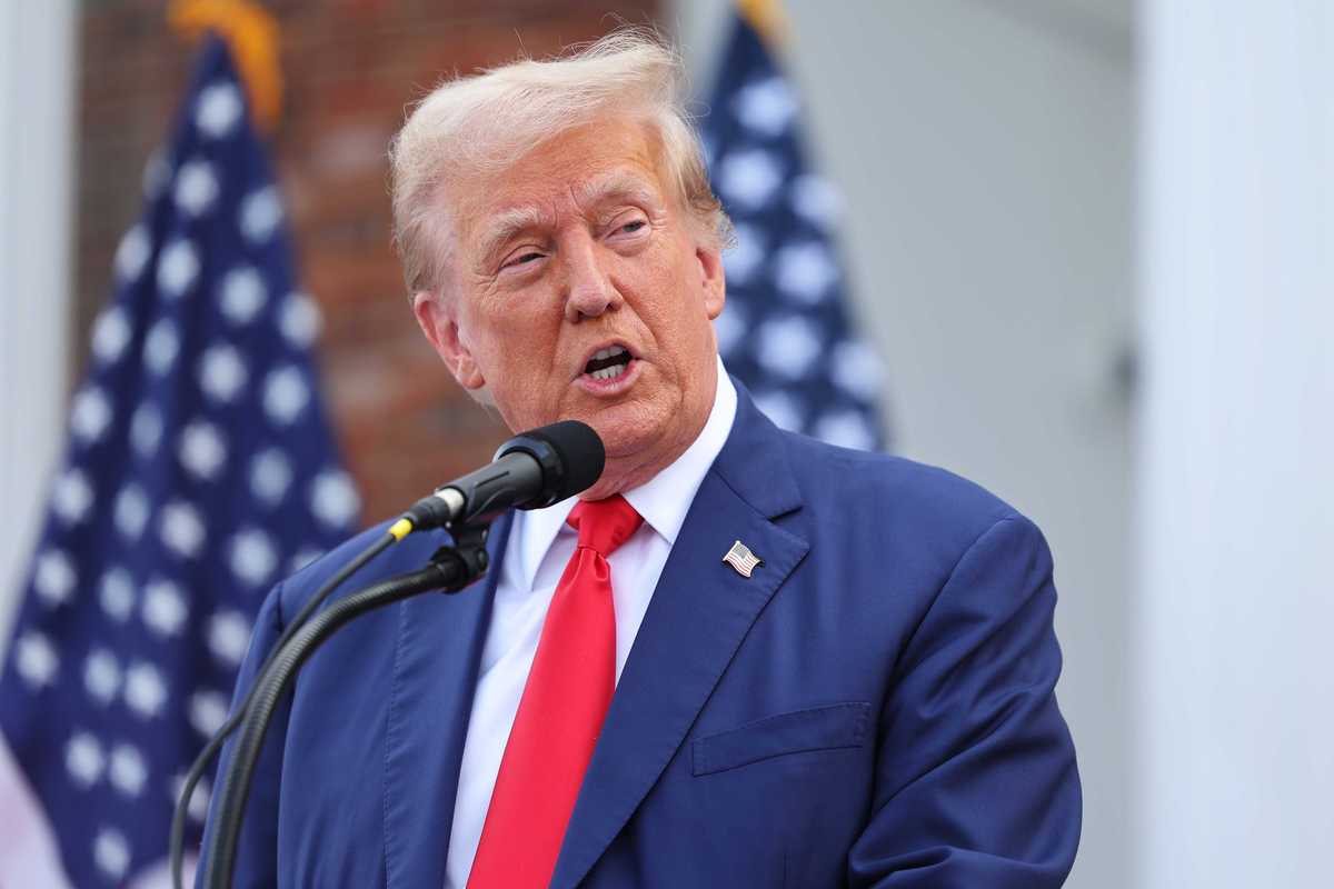 Donald Trump, wearing a blue suit and red tie, speaks into a microphone.
