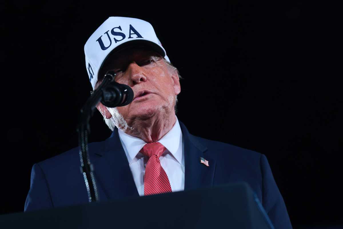 Donald Trump, wearing a blue suit and white cap, speaks into a microphone at a rally in North Carolina.