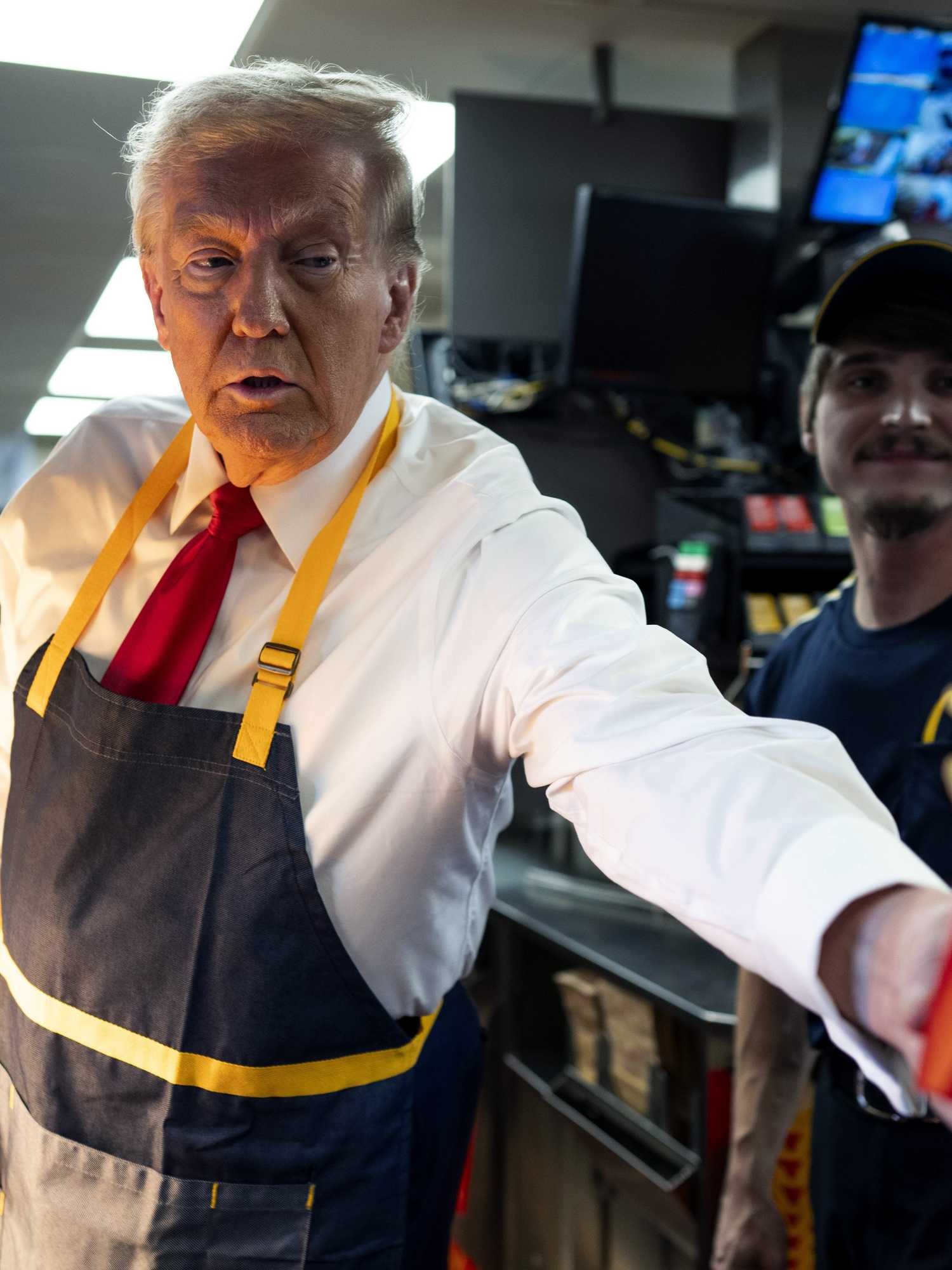 Donald Trump wearing a grey and yellow McDonald's apron hands out some fries to a reporter inside the restaurant.
