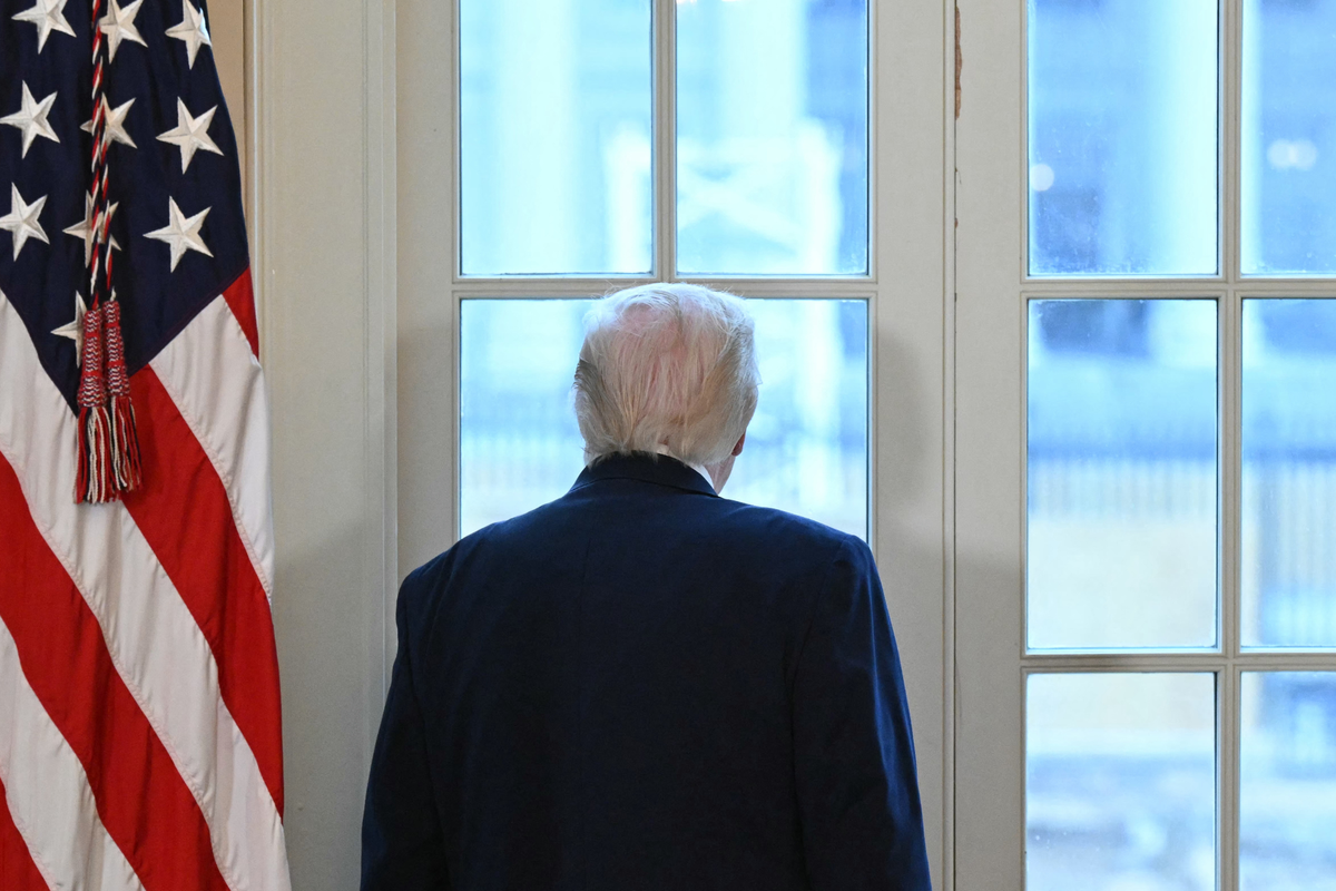 Donald Trump with his back to the camera, looking out of a window in the White House.