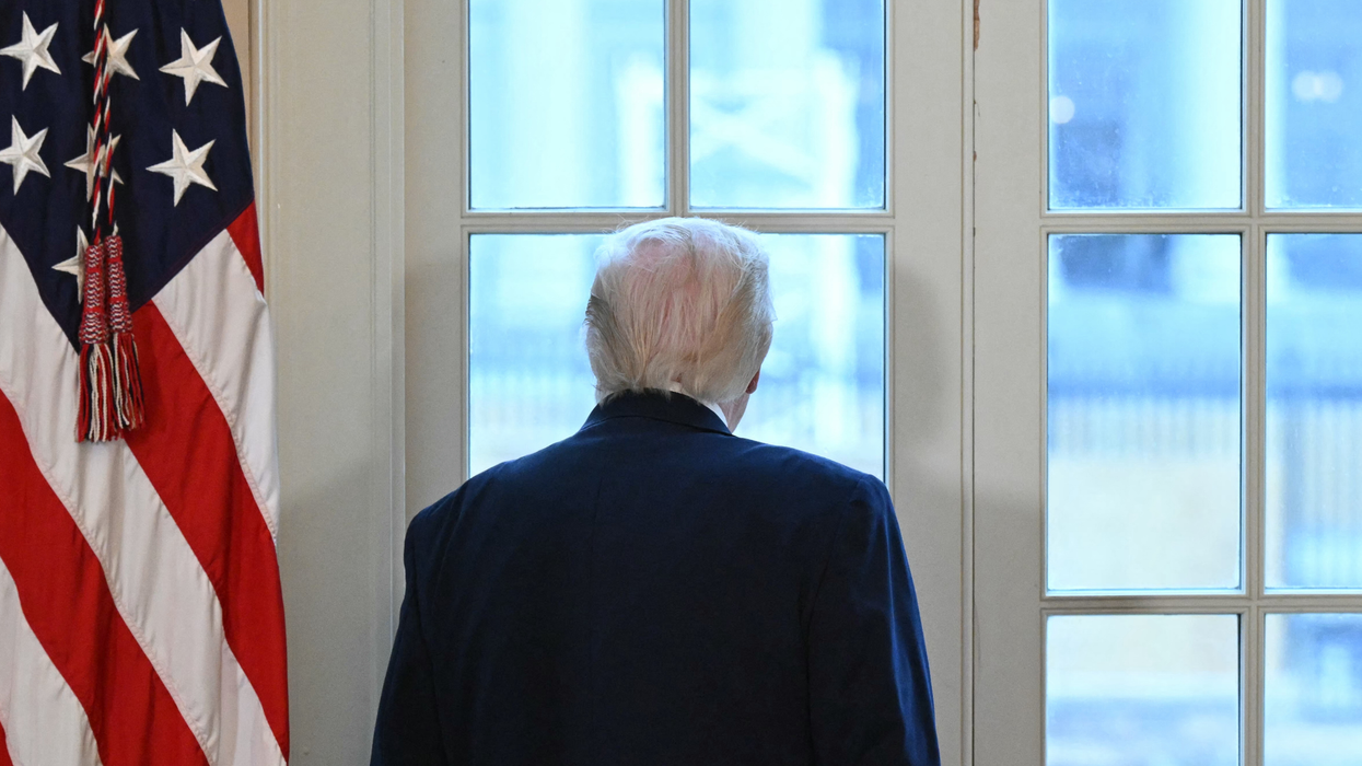 Donald Trump with his back to the camera, looking out of a window in the White House.