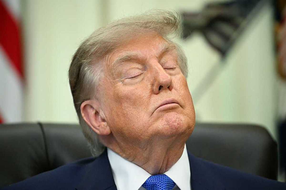 Donald Trump with his eyes closed sitting behind the Resolute Desk in the Oval Office.