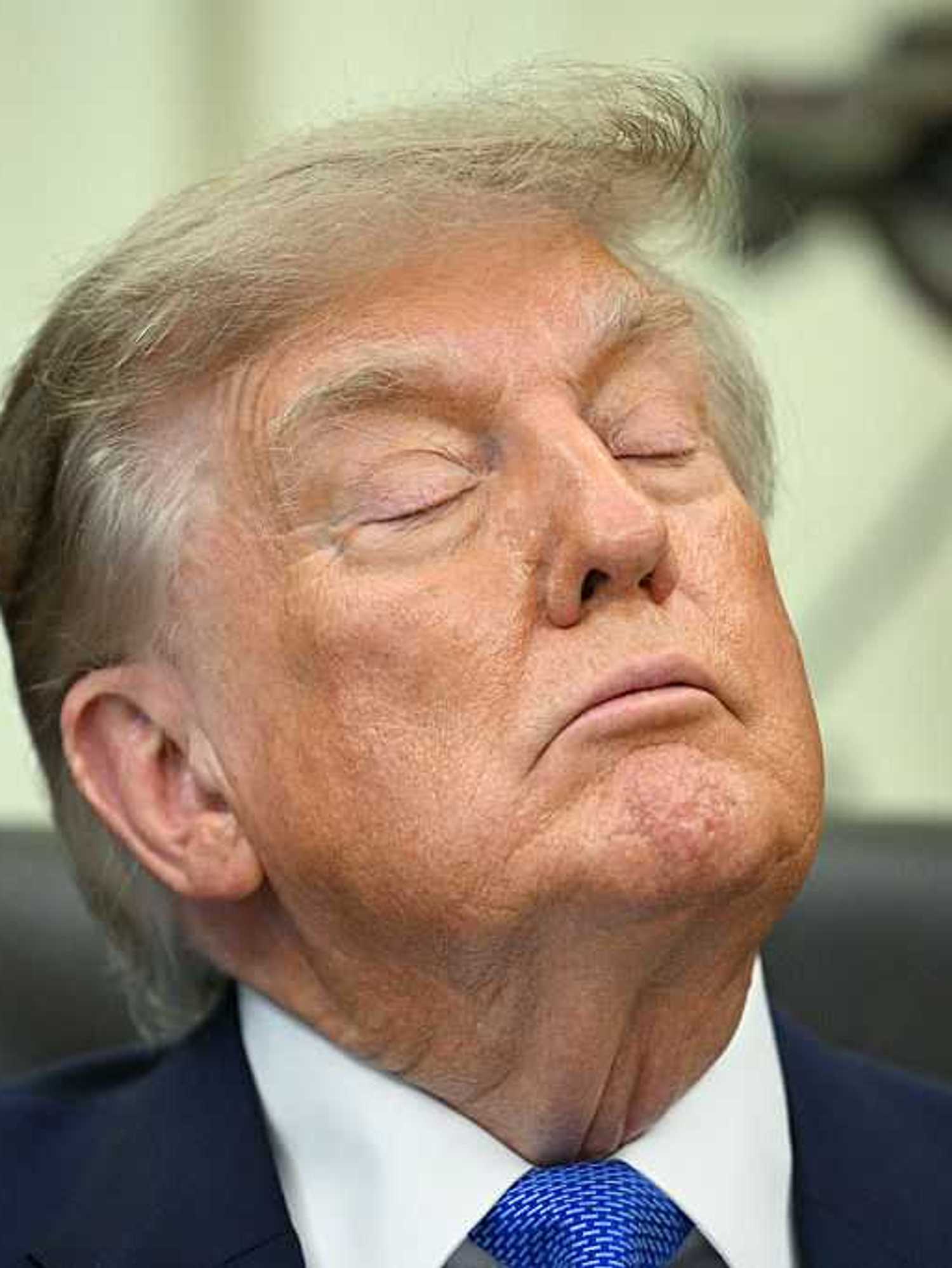 Donald Trump with his eyes closed sitting behind the Resolute Desk in the Oval Office.
