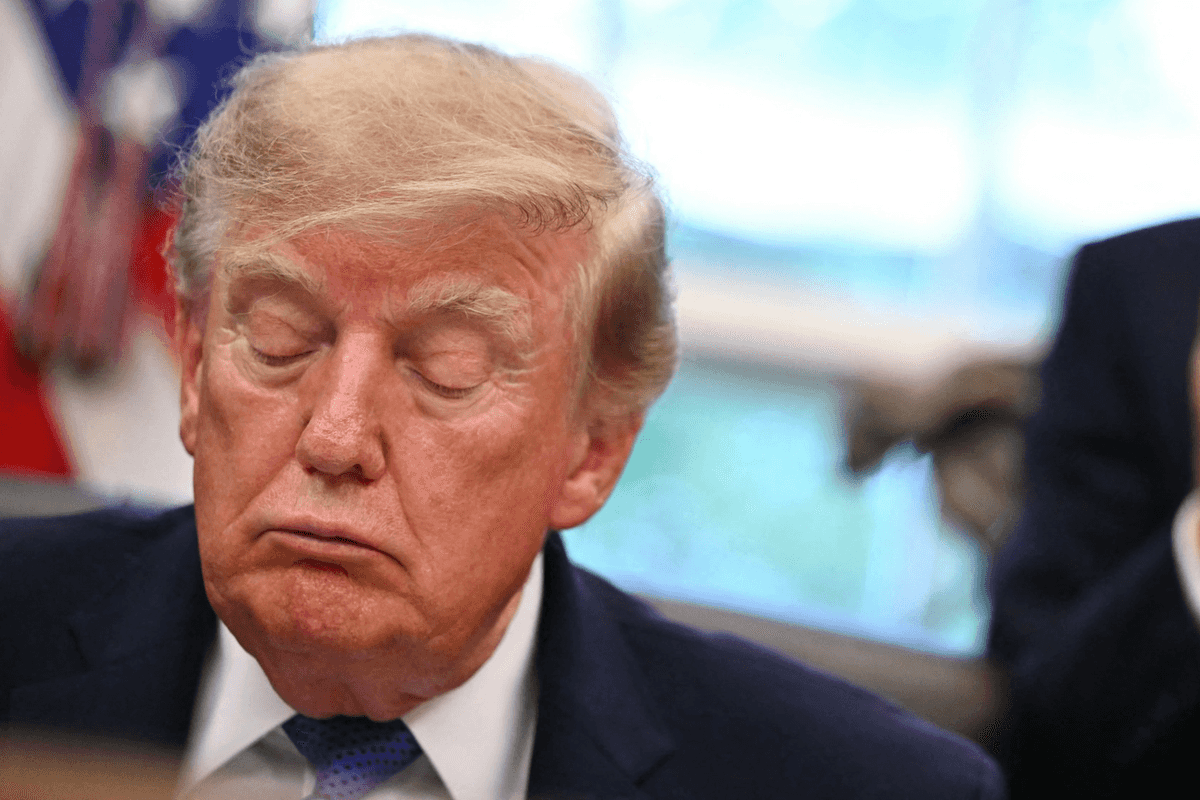 Donald Trump with his eyes closed, sitting behind the Resolute Desk in the Oval Office.