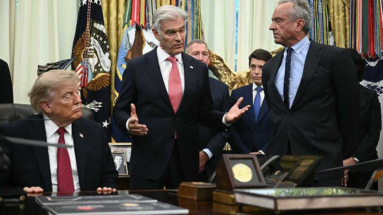 Dr Mehmet Oz speaking in the Oval Office, with Robert F. Kennedy Jr to the left of him and Donald Trump on his right, sitting at the Resolute Desk.