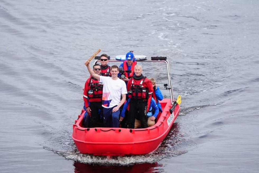 Duncan Scott holding the King's Baton aloft and smiling while on a boat on a river