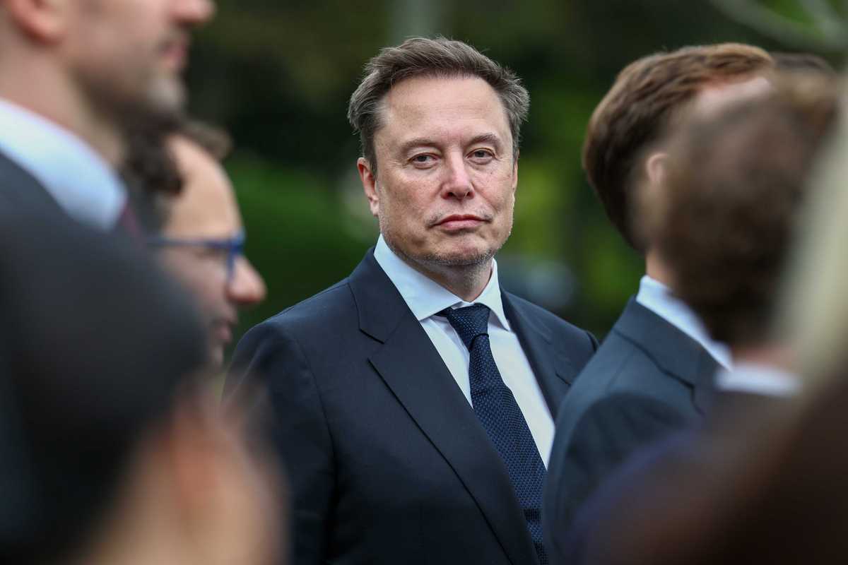 Elon Musk looking directly at the camera, while several other men look straight ahead, to the right of the photo.