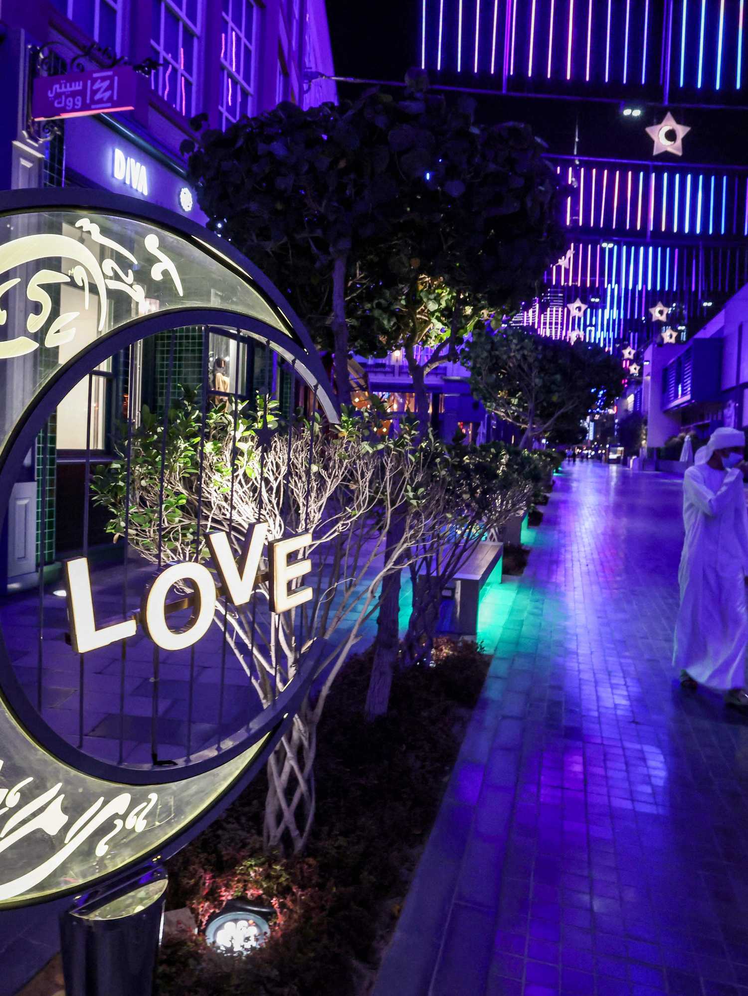 Emirati youths walk past a large lit decoration in the shape of a crescent moon bearing calligraphic text in Arabic reading "Ramadan Mubarak", at the City Walk district of Dubai at the start of the first night of the Muslim holy fasting month of Ramadan on April 12, 2021.