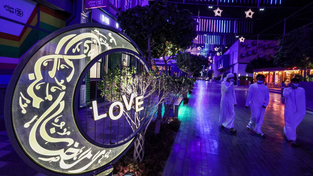 Emirati youths walk past a large lit decoration in the shape of a crescent moon bearing calligraphic text in Arabic reading "Ramadan Mubarak", at the City Walk district of Dubai at the start of the first night of the Muslim holy fasting month of Ramadan on April 12, 2021.
