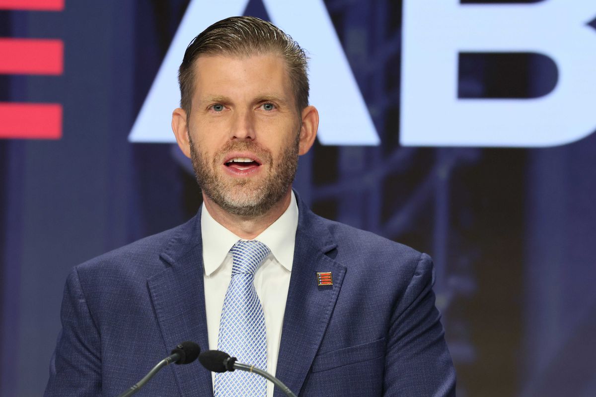 Eric Trump speaks behind a lectern, wearing a blue suit.