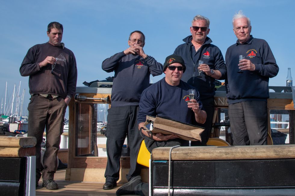 Five men on board a boat, each with a glass of champagne