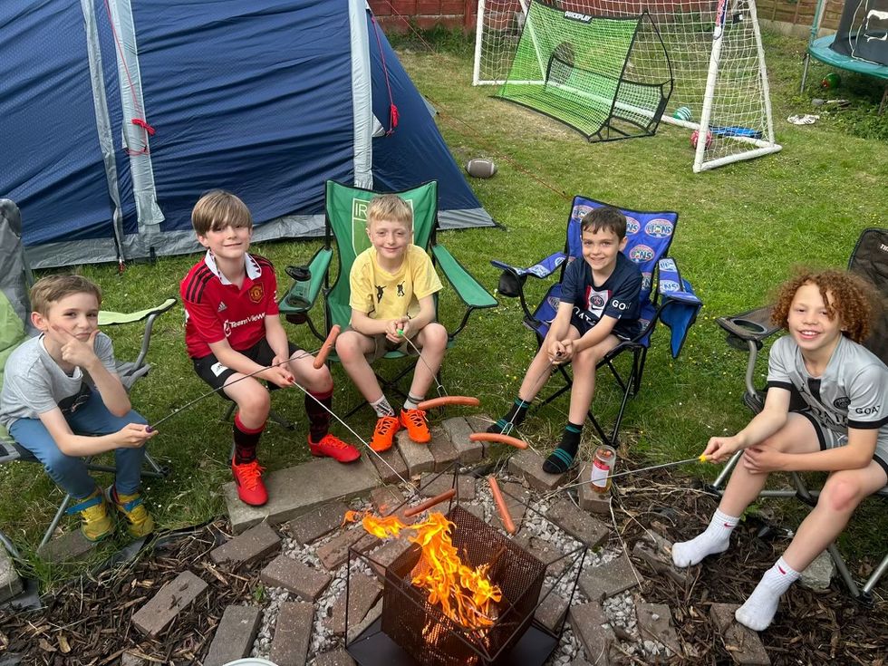 Five of the boys sat round a campfire holding sausages