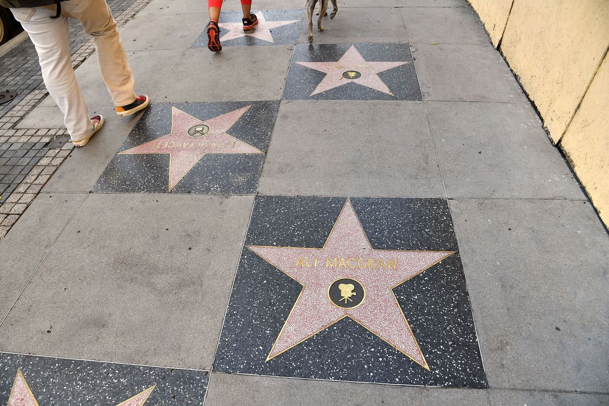 Four marble stars embedded in a grey pavement. There is writing on them, but only the nearest is distinguishable, the name "ALI MACGRAW"