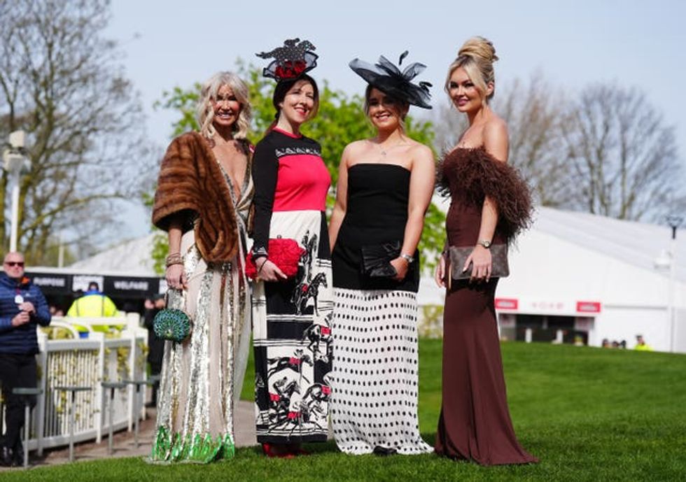 Four women at Aintree, one in a fur stole, one in a red and black gown, one in a strapless black and white gown and one in a chocolate brown dress with feather detail