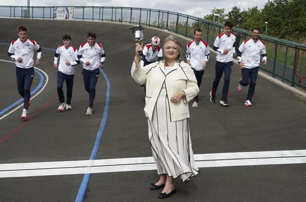 Frances Connolly ringing a bell while standing at the finish line of a track at Middlesbrough Velodrome as men in tracksuits run towards her
