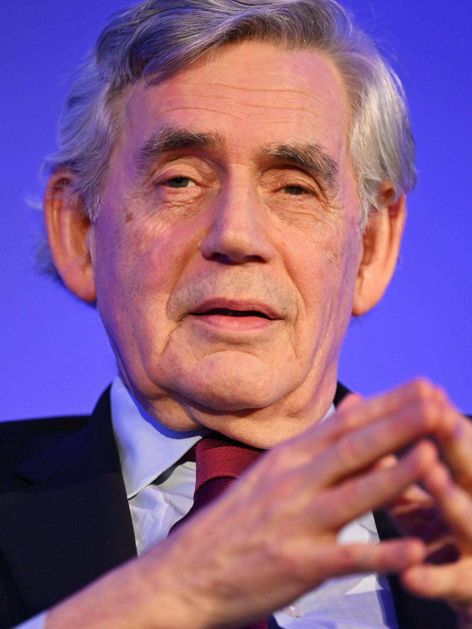 Gordon Brown, wearing a black suit and with his fingers arched together in front of him.