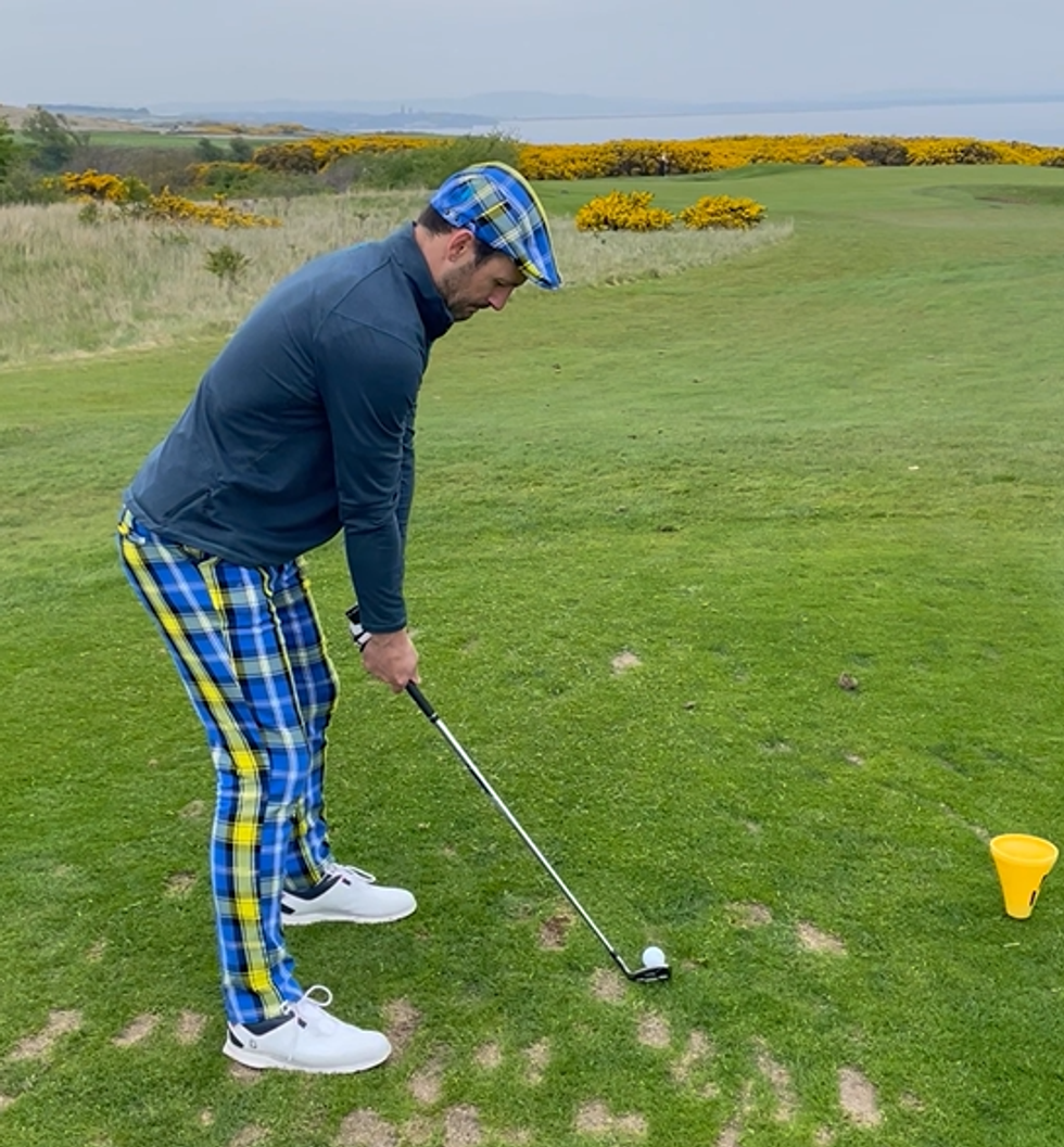 Graeme Smeaton teeing off, dressed in vibrant blue and yellow tartan trousers and cap, and a blue top