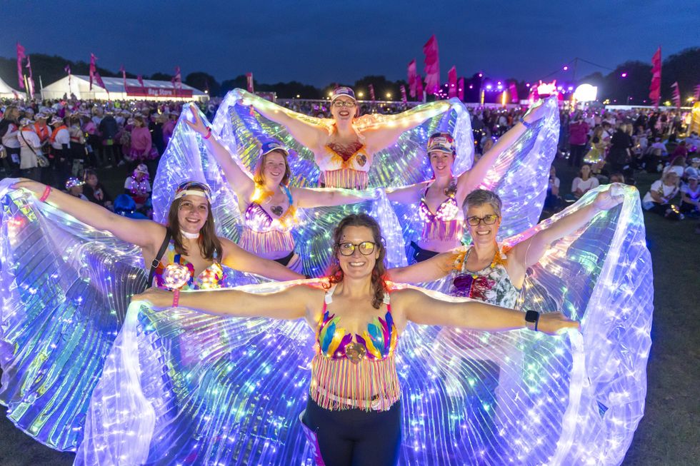 Group of women wear decorated bras and outstretch a lit-up cape