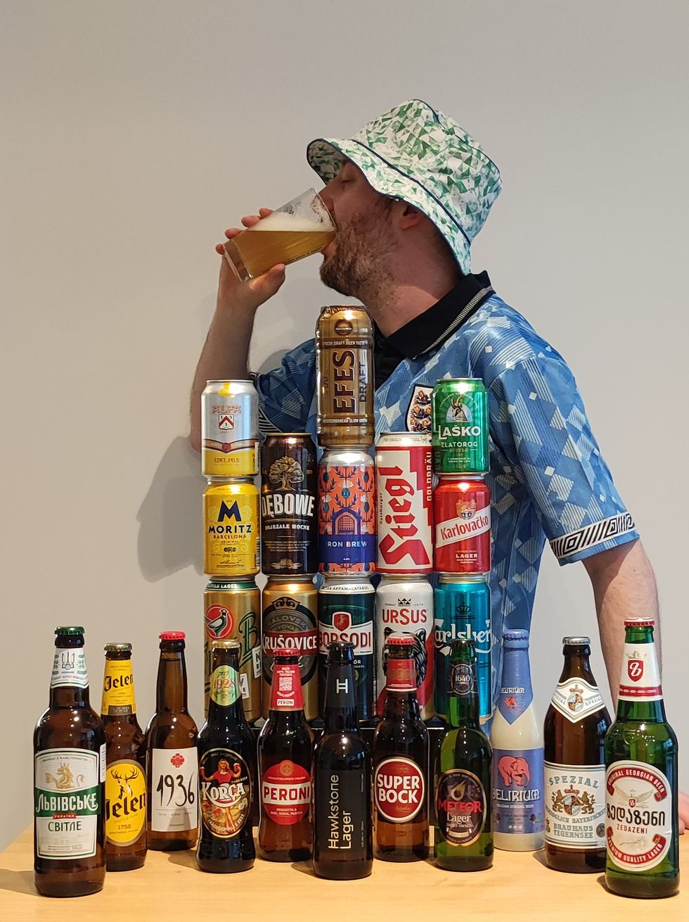 Gus Hully drinking a beer and standing in front of a table where the 24 beers are placed