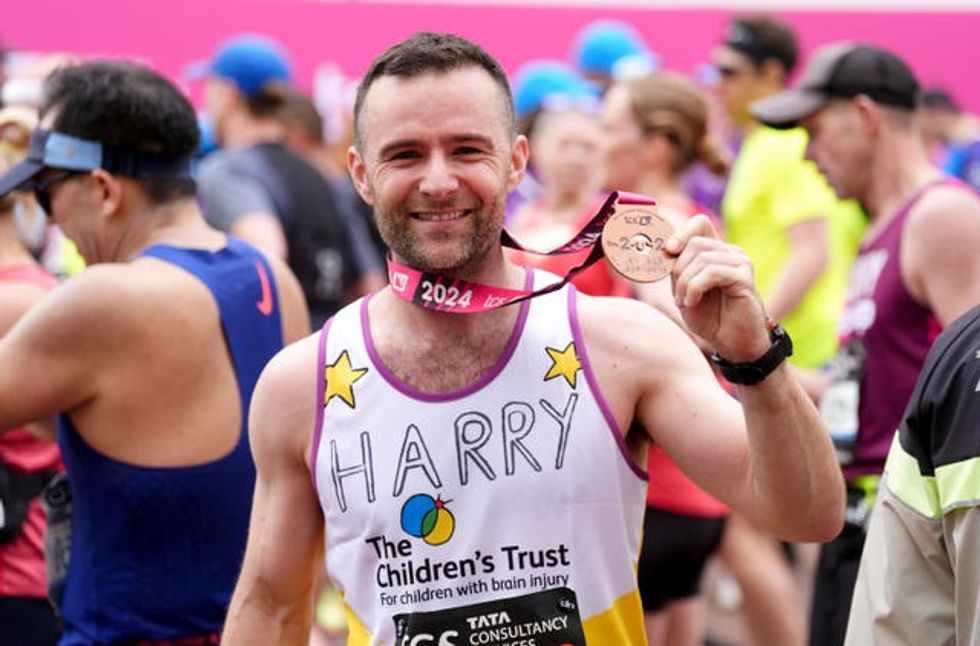 Harry Judd smiling and holding up his medal after finishing the London Marathon in 2024