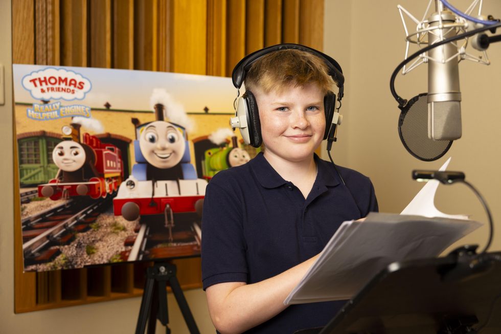 Harry Sparkes wearing a black polo and headphones standing in front of a microphone and Thomas The Tank Engine poster